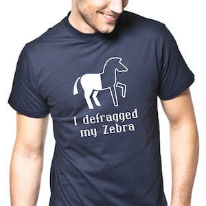 Könnte beinhalten: Ein marineblaues T-Shirt mit einer weißen Grafik eines Zebras, dem die Hälfte seines Körpers fehlt. Der Text "I defragged my Zebra" ist unter der Grafik aufgedruckt.