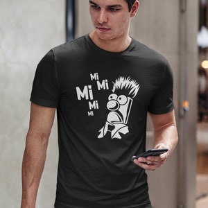 Könnte beinhalten: Ein schwarzes T-Shirt mit einem weißen Aufdruck eines Comic-Charakters mit dem Text "Mi Mi Mi Mi Mi" auf der Vorderseite.
