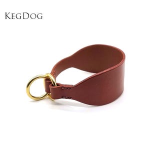 May include: A brown leather dog collar with a gold metal ring. The collar is a half-choke style, meaning it tightens when pulled.