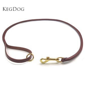 Puede incluir: Una correa de perro de cuero marrón con un clip de metal dorado y un anillo de metal dorado.