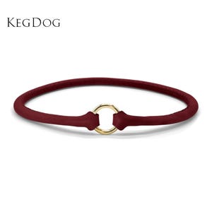May include: A deep red, rounded collar featuring the text KEGDOG in the upper left corner. The collar is constructed from a smooth, matte material and is secured at the front center with a polished, circular gold-toned metal ring connector.