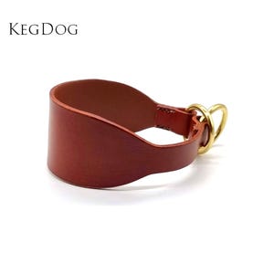 May include: A brown leather dog collar with a brass buckle and D-ring. The collar is designed to fit snugly around the dog's neck and is made of high-quality leather.