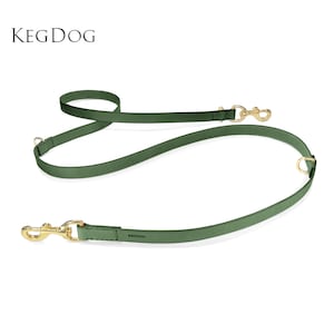 Puede incluir: Una correa para perro de color verde bosque con herrajes de metal dorado, que incluye dos ganchos giratorios y dos anillos en D. La correa tiene grabado el texto KEGDOG. El diseño permite ajustar la longitud y ofrece múltiples puntos de enganche.
