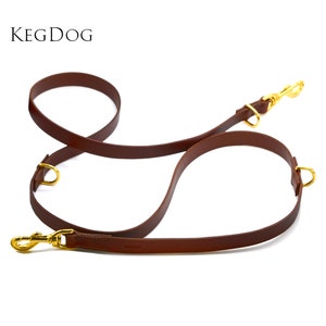 May include: A brown leather dog leash with two gold metal clips and a gold metal ring. The leash is designed to be used with two dogs.