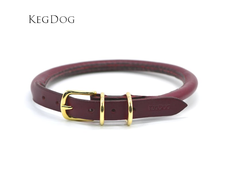 May include: A burgundy leather dog collar with a gold buckle and two gold rings. The collar is embossed with the text "KEGDOG".