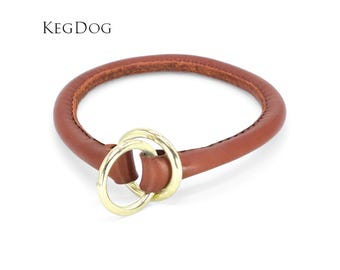 May include: A brown leather dog collar with a rounded, padded design and two interlocking gold-tone metal rings at the front. The text KEGDOG is printed in black in the upper left corner of the image, above the circular collar.