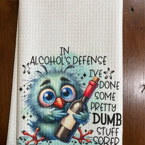 May include: White kitchen towel with a whimsical design. It features a cartoon bird holding a wine bottle, with the text "IN ALCOHOL'S DEFENSE I'VE DONE SOME PRETTY DUMB STUFF SOBER."
