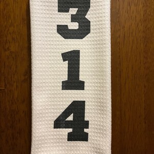 以下が含まれることがあります： 白地のキッチンタオルに黒で314の数字がプリントされています。タオルは質感のある表面で、茶色の木のドアに掛けられています。