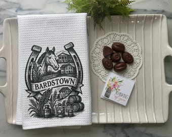 Puede incluir: Toalla de cocina blanca con tejido de gofres con un gráfico en blanco y negro de un caballo, una herradura y la palabra "Bardstown". La toalla está en una bandeja blanca con bombones y una pequeña tarjeta que dice "Thinking of you".