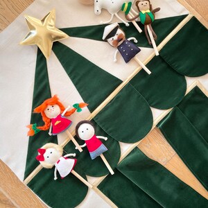 May include: A handmade Christmas tree-shaped decoration with a gold star and green velvet accents. The tree is adorned with felt puppets, including a sailor, a monkey, a horse, and several dolls. The puppets are attached to wooden sticks.