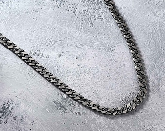 May include: A silver chain necklace with black accents. The chain is a curb style with a flat, rectangular link.