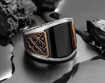 May include: A silver ring with a black onyx stone and a rose gold band. The band is decorated with a geometric pattern and black stones.