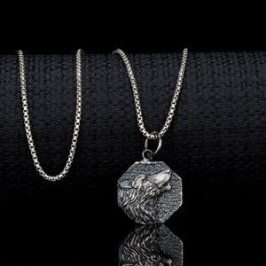 May include: A silver chain necklace with a pendant featuring a detailed wolf head design. The pendant is octagonal in shape and has a textured surface.