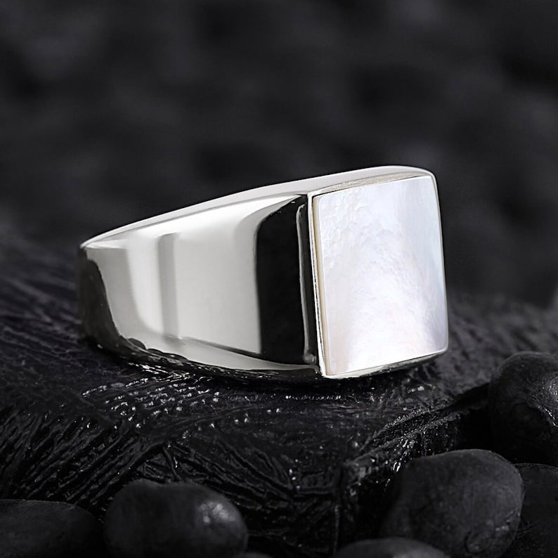 May include: A silver ring with a square white mother-of-pearl inlay.