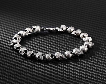 May include: A silver skull bracelet with multiple skull charms linked together. The bracelet is on a black textured background.