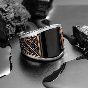 May include: A silver ring with a black stone and a decorative pattern of black stones set in a gold frame.