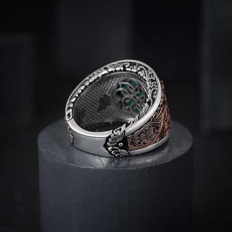 May include: A silver ring with intricate floral designs and a green gemstone set in the center. The ring has a rose gold band.