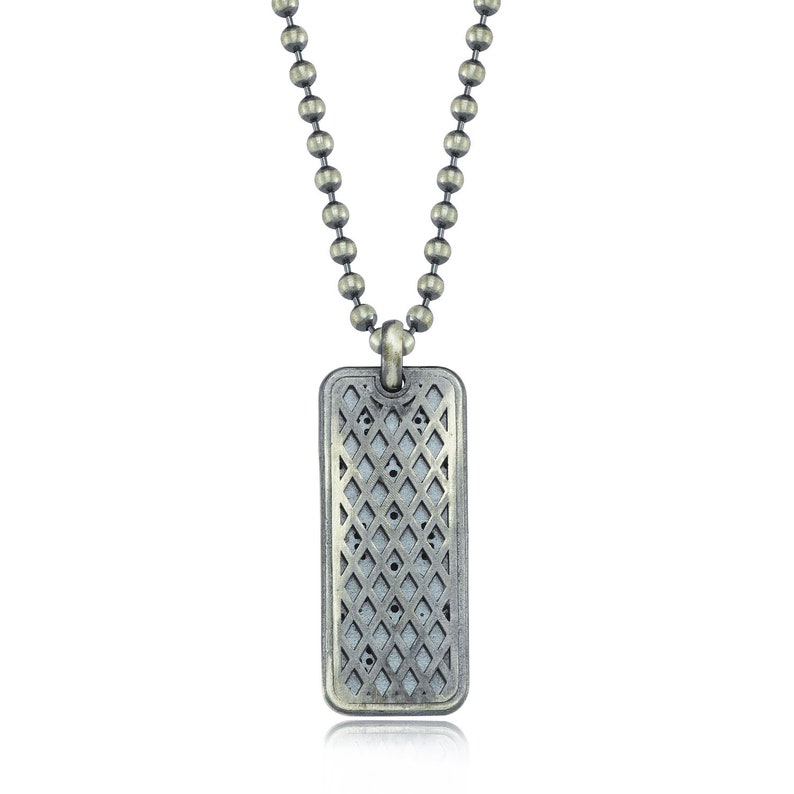 Puede incluir: Un collar de cadena de plata con un colgante rectangular con un patr&oacute;n geom&eacute;trico. El colgante tiene un acabado desgastado.