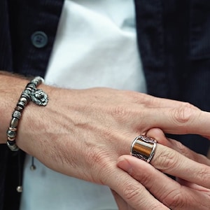 May include: A silver bracelet with a lion head charm and a brown and silver ring with a tiger eye stone.