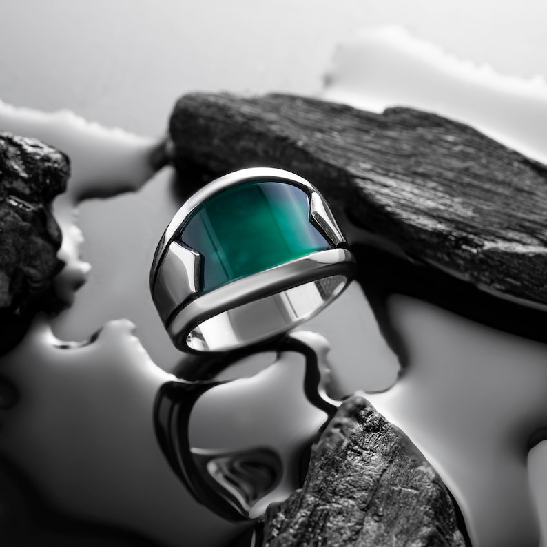 May include: A silver ring with a green gemstone set in a wide band.