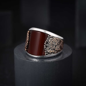 May include: A silver ring with a red agate stone and intricate floral designs in rose gold.