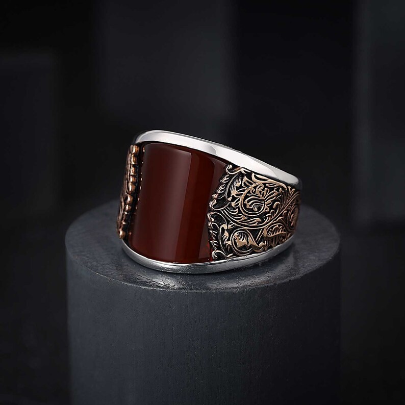 May include: A silver ring with a red agate stone and intricate floral designs in rose gold.