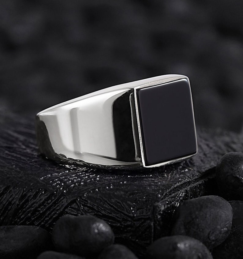 May include: A silver ring with a black square gemstone.