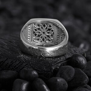 May include: A silver ring featuring a Celtic knot design. The ring is shown from the inside, showcasing the intricate details of the knot.