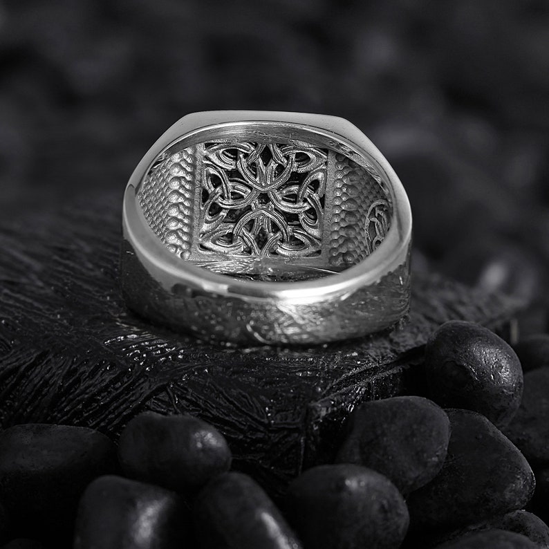May include: A silver ring featuring a Celtic knot design. The ring is shown from the inside, showcasing the intricate details of the knot.