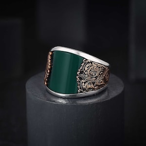May include: A silver ring with a green stone and intricate gold filigree design.
