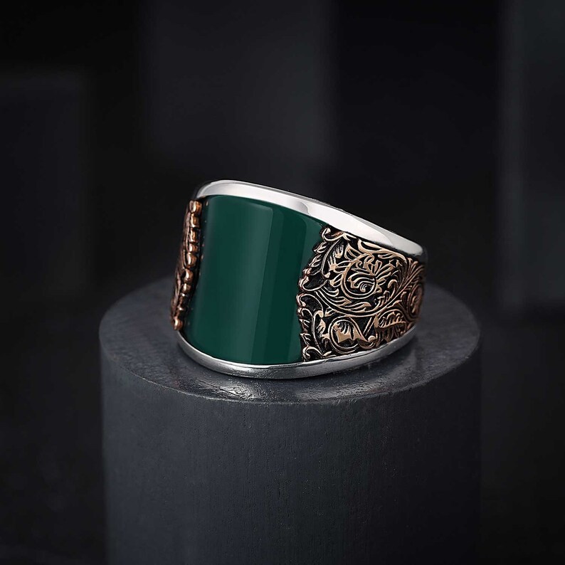 May include: A silver ring with a green stone and intricate gold filigree design.
