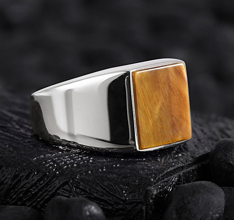 May include: A silver ring featuring a square tiger's eye gemstone.