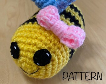 May include: A crocheted bee toy with yellow and black stripes, black eyes, and a pink bow. The bee has blue wings.