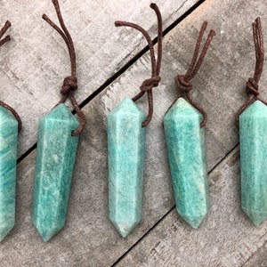 May include: Five Amazonite crystal pendants with brown cord necklaces. The pendants are a light teal color with white veining and a pointed bottom. The cords are knotted at the top.