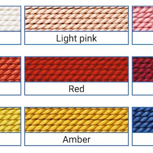May include: A colour chart displaying nine different shades of yarn. The colours include white, light pink, dark pink, coral, red, garnet, yellow, amber, and blue. Each colour is shown in a rectangular box with the colour name below.