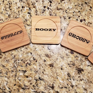 Puede incluir: Cinco posavasos cuadrados de madera con bordes redondeados y un hueco circular. Cada posavasos tiene una palabra diferente inscrita en letras negras: Tipsy, Fuddled, Boozy, Groggy y Elevated.