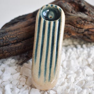 Può includere: Una pipa in ceramica con base bianca e strisce blu. La pipa ha un'apertura rotonda nella parte superiore.