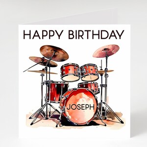 May include: A birthday card with a watercolour illustration of a red drum kit, complete with cymbals. The words "HAPPY BIRTHDAY" are at the top, and the name "JOSEPH" is on the bass drum. The background is white.