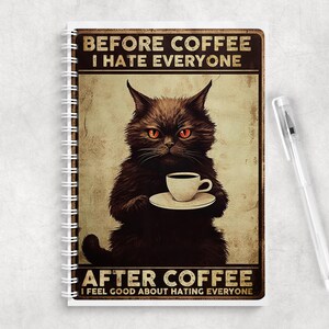 May include: A spiral-bound notebook featuring a black cat with orange eyes holding a white coffee cup. The text reads: BEFORE COFFEE I HATE EVERYONE and AFTER COFFEE I FEEL GOOD ABOUT HATING EVERYONE. A clear plastic pen lies next to the notebook.