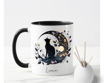 May include: White ceramic mug with a black rim and handle. The mug features a black silhouette of a cat sitting on a crescent moon with floral details and a starry background. The text "Luna" is printed on the bottom of the mug.