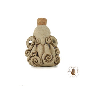 Op de afbeelding: Een klein keramiek flesje in de vorm van een octopus met een kurkstop. De fles is beige met bruine details.