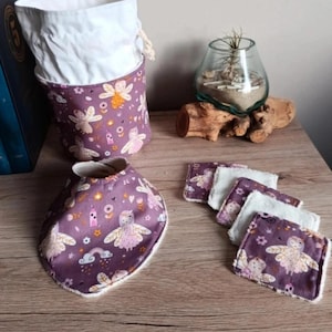 Puede incluir: Un conjunto de accesorios para bebés con temática de hadas. Incluye un babero, varias toallitas pequeñas y un recipiente de almacenamiento. Los artículos presentan una tela morada con un patrón de hadas y arcoíris, y detalles en blanco.
