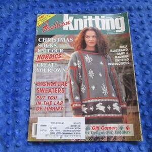 May include: Fashion Knitting magazine issue featuring a grey sweater with white snowflake and rabbit patterns, red trim, and text including Christmas Socks, Knit Our Nordics, Signature Sweaters, and Gift Corner: Knit Designs For Toddlers.
