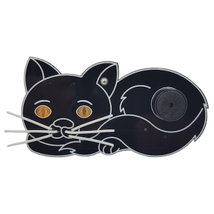 Op de afbeelding: Zwarte kattenuitsparing met witte snorharen en gele ogen. De kat ligt met zijn staart om zijn lichaam gekruld. Er is een kleine zwarte cirkel op de rug van de kat.