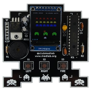 Puede incluir: Una placa de circuito impreso en blanco y negro con una pequeña pantalla LCD que muestra un videojuego retro. El juego presenta una nave espacial disparando a naves espaciales extraterrestres. La placa de circuito impreso tiene botones etiquetados como "IZQUIERDA", "DERECHA" y "FUEGO". El texto "SCORE 00000 HI-SCORE 00070" se muestra en la pantalla.