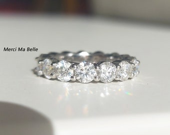 May include: A silver band ring with a row of round, clear gemstones. The ring is on a white surface.