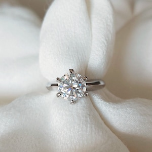 May include: A silver ring with a large, clear, round diamond set in a six-prong setting.