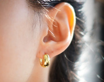 May include: Close-up of a gold-colored hoop earring. The earring is a small, rounded shape, and it is worn on the ear. The earring has a shiny, polished finish.
