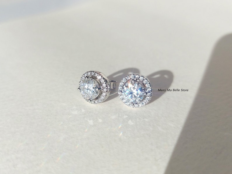 May include: A pair of silver stud earrings with a round, clear stone surrounded by a halo of smaller stones.