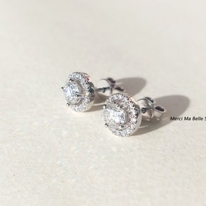 May include: A pair of silver stud earrings with a round, clear crystal center surrounded by a halo of smaller crystals.
